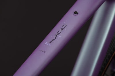 Detail eines violetten Fahrradrahmens mit der Aufschrift NUROAD PRO und der Größe M. Detail eines violetten Fahrradrahmens mit der Aufschrift NUROAD PRO und der Größe M.