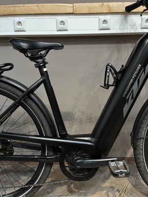 Schwarzes E-Bike mit Flaschenhalter und KTM-Logo, stehend vor Steckdosen. Schwarzes E-Bike mit Flaschenhalter und KTM-Logo, stehend vor Steckdosen.