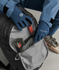 Blaue ORTOVOX-Handschuhe werden in einen Rucksack mit einem orangefarbenen Gegenstand gesteckt.