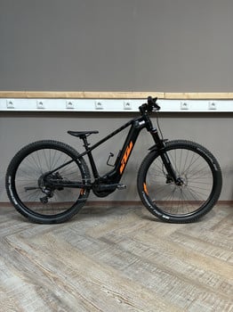 Schwarzes E-Bike mit orangefarbenen Details vor dunklem Hintergrund.