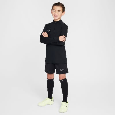 Junge in schwarzer Fußballkleidung mit weißem Nike-Logo, Arme verschränkt.