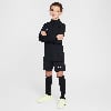 Junge in schwarzer Fußballkleidung mit weißem Nike-Logo, Arme verschränkt.
