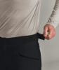 Ein Mann passt den Klettverschluss an seiner schwarzen Hose unter einem beigen Hemd an.
