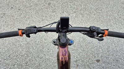 E-Bike-Lenker mit Display und orangefarbenen Griffen auf Asphalt. E-Bike-Lenker mit Display und orangefarbenen Griffen auf Asphalt.