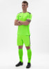 Ein Mann in einem neongrünen Fußballtrikot und Shorts steht mit verschränkten Armen.