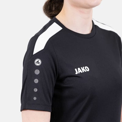 Frau in schwarzem T-Shirt mit weißen Streifen an den Schultern und JAKO-Logo. Frau in schwarzem T-Shirt mit weißen Streifen an den Schultern und JAKO-Logo.