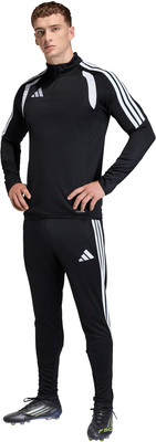 Ein Mann im schwarzen Adidas-Anzug mit weißen Streifen und Fußballschuhen.