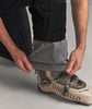Ein Mann zieht einen Skischuh über seine Hose mit Innenmanschette.