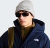 Ein Mann in einer Winterjacke, Mütze und Sonnenbrille trägt einen Rucksack.