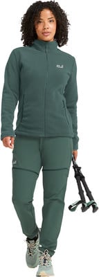 Eine Frau in einem dunkelgrünen Fleece und Hose hält Wanderstöcke. Eine Frau in einem dunkelgrünen Fleece und Hose hält Wanderstöcke.