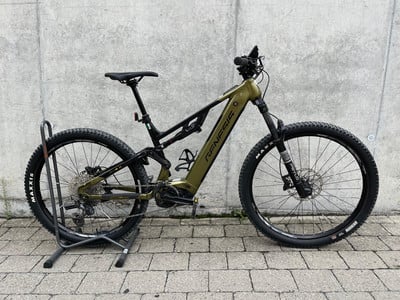 Grünes Genesis E-Bike mit Federung, Ständer und Betonwand im Hintergrund. Grünes Genesis E-Bike mit Federung, Ständer und Betonwand im Hintergrund.