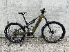 Grünes Genesis E-Bike mit Federung, Ständer und Betonwand im Hintergrund.
