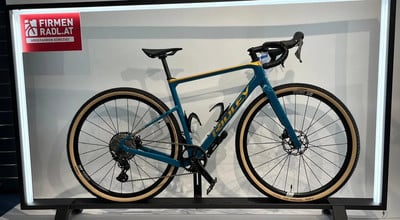 Ein blaues Ridley Gravelbike mit beige Reifen und goldenen Akzenten.