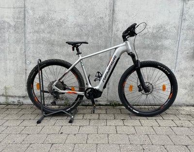 Silbernes Genesis E-Bike auf einem Ständer vor einer Betonwand.