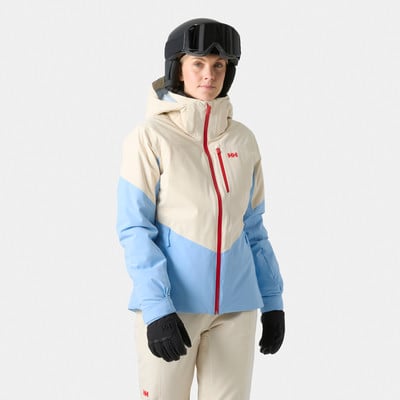 Frau in einer beige-blauen Skijacke mit rotem Reißverschluss und Helm. Frau in einer beige-blauen Skijacke mit rotem Reißverschluss und Helm.
