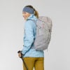 Frau mit Rucksack und Wanderstöcken vor grauem Hintergrund.