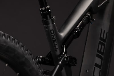 Detail des Hinterbaus eines schwarzen Mountainbikes mit Dämpfer und Aufschrift ONE44. Detail des Hinterbaus eines schwarzen Mountainbikes mit Dämpfer und Aufschrift ONE44.