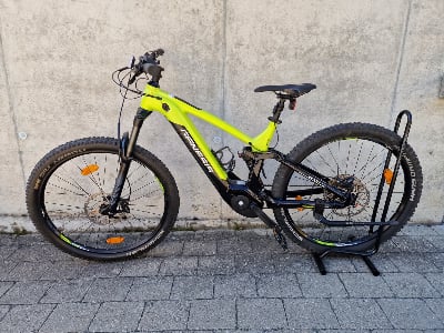 Ein grünes Genesis E-Bike mit Federung steht auf einem Ständer vor einer Wand. Ein grünes Genesis E-Bike mit Federung steht auf einem Ständer vor einer Wand.