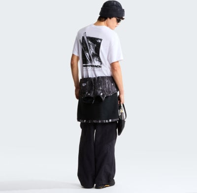 Mann in weißem T-Shirt mit Aufdruck und schwarzer Hose mit Weste um die Taille.