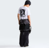 Mann in weißem T-Shirt mit Aufdruck und schwarzer Hose mit Weste um die Taille.