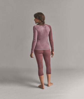 Eine Frau in einem rosa Langarmshirt und Dreiviertel-Leggings steht mit dem Rücken zur Kamera. Eine Frau in einem rosa Langarmshirt und Dreiviertel-Leggings steht mit dem Rücken zur Kamera.
