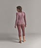 Eine Frau in einem rosa Langarmshirt und Dreiviertel-Leggings steht mit dem Rücken zur Kamera.