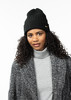 Eine Frau mit lockigem Haar trägt eine schwarze Mütze und einen grauen Pullover.