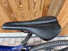 Schwarzer Fahrradsattel mit perforiertem Muster auf Holzuntergrund.