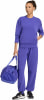 Eine Frau in violetter Kleidung hält eine blaue Tasche und trägt schwarze Schuhe.