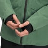 Detail der Hände in schwarzen Handschuhen mit Daumenöffnungen unter einer grünen Jacke.