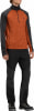 Ein Mann in einem orange-grauen Langarmshirt und schwarzer Hose.