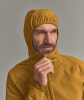 Ein Mann in einer gelben Kapuzenjacke richtet den Kragen am Kinn.