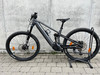 Graues E-Mountainbike auf einem Ständer vor einer Betonwand.