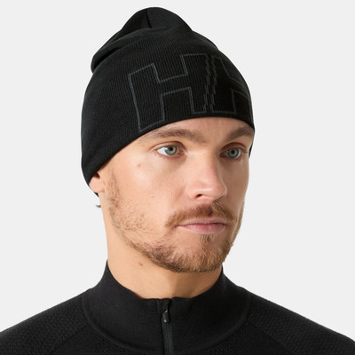 Egy férfi fekete HH logós sapkában és fekete, magas nyakú pulóverben.