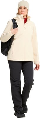 Eine Frau in einer cremefarbenen Jacke und schwarzer Hose mit Rucksack.