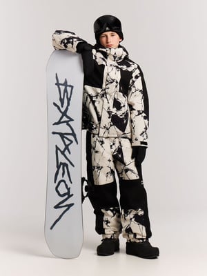 Junger Snowboarder in schwarz-weißer Kombi und Brille mit Brett. Junger Snowboarder in schwarz-weißer Kombi und Brille mit Brett.