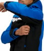 Ein Mann schließt den Reißverschluss einer blau-schwarzen Skijacke mit weißen Streifen.