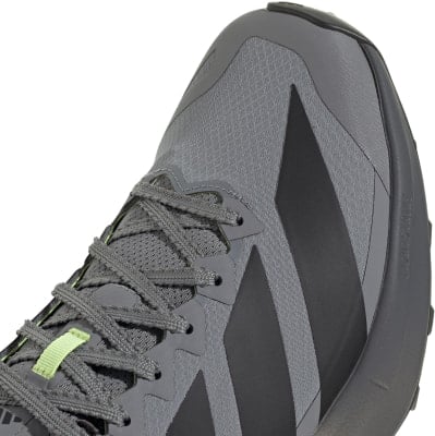Grauer Laufschuh mit dunklen Streifen und grünen Schnürsenkeldetails. Grauer Laufschuh mit dunklen Streifen und grünen Schnürsenkeldetails.
