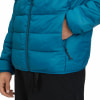 Blaue Daunenjacke mit schwarzer Hose und Hand in der Tasche.