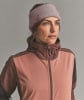 Frau mit rosafarbenem Stirnband und Jacke vor grauem Hintergrund.