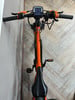 Orange E-Bike mit Display und schwarzem Sattel auf Holzboden.