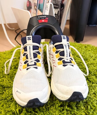 Weiße Salomon-Laufschuhe mit blauen und gelben Details auf einem grünen Teppich. Weiße Salomon-Laufschuhe mit blauen und gelben Details auf einem grünen Teppich.