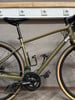 Ein goldenes Fahrrad mit schwarzem Sattel und schwarzen Pedalen steht an der Wand.