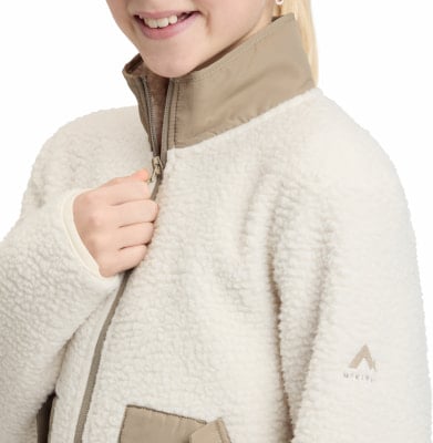 Ein Mädchen schließt eine cremefarbene Fleecejacke mit braunem Kragen. Ein Mädchen schließt eine cremefarbene Fleecejacke mit braunem Kragen.