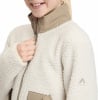 Ein Mädchen schließt eine cremefarbene Fleecejacke mit braunem Kragen.
