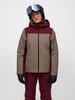 Eine Skifahrerin in einer bunten Jacke und einem Helm mit Brille posiert vor weißem Hintergrund.