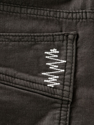 Detail einer Naht an dunklen Hosen mit weißem EKG-Muster. Detail einer Naht an dunklen Hosen mit weißem EKG-Muster.