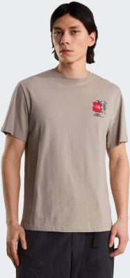 Mann in einem beigen T-Shirt mit Aufdruck auf der Brust und schwarzer Hose.