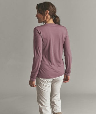 Frau in einem rosafarbenen Langarmshirt und beiger Hose vor grauem Hintergrund. Frau in einem rosafarbenen Langarmshirt und beiger Hose vor grauem Hintergrund.