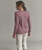 Frau in einem rosafarbenen Langarmshirt und beiger Hose vor grauem Hintergrund.